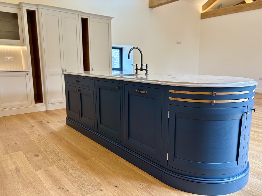 Bespoke blue curved kitchen island with marble-effect worktop, integrated sink, brass details and cream cabinetry by 21 Kitchens in Ayrshire.