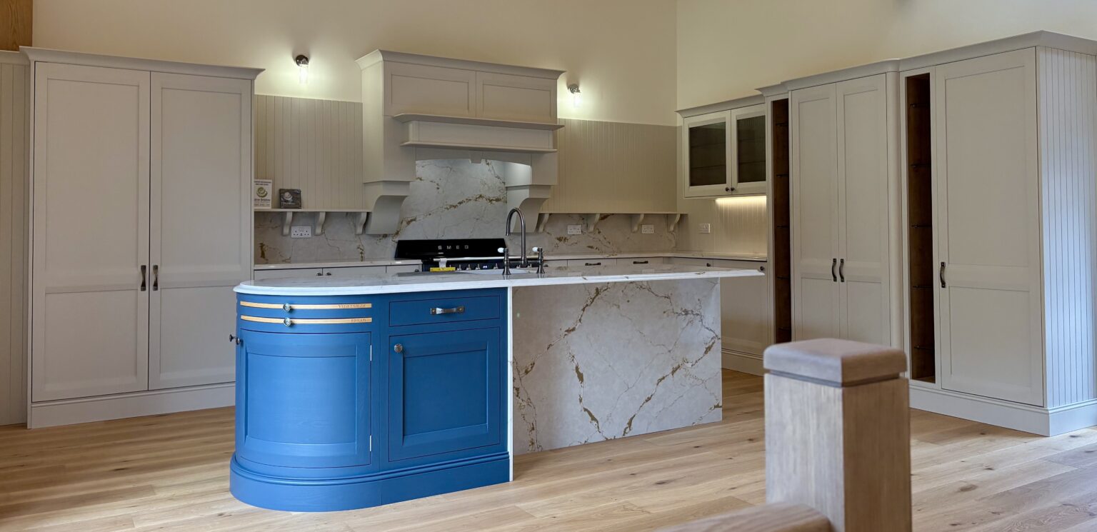 Bespoke kitchen design with blue curved island, marble-effect worktops, cream cabinetry and classic detailing by 21 Kitchens in Ayrshire.