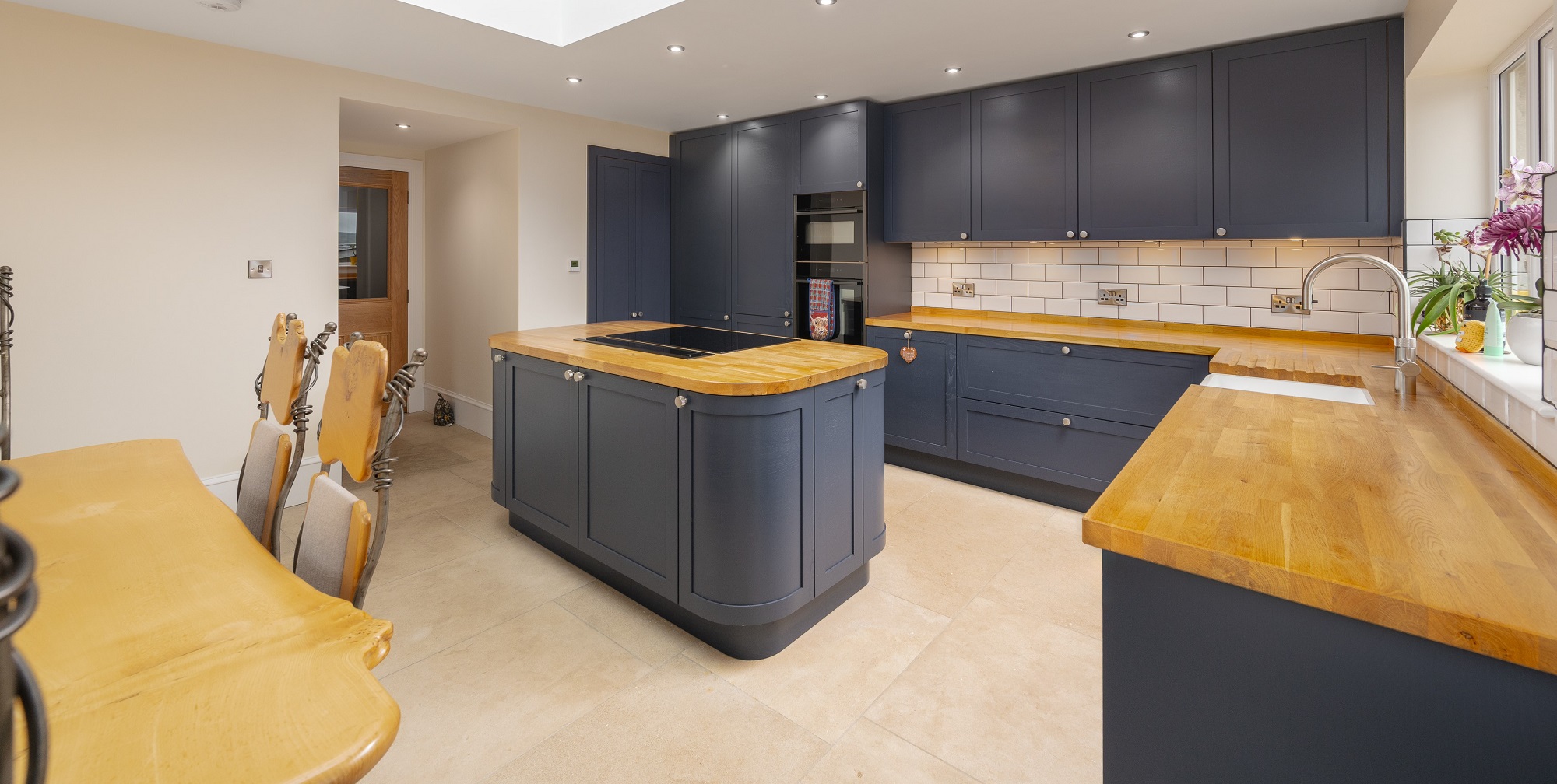 Dark blue shaker kitchen with oak worktops, central island and white metro tiles by 21 Kitchens in Ayrshire