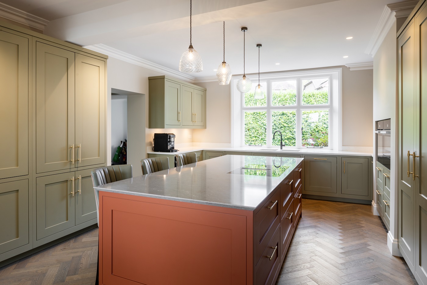 British painted shaker kitchen with sage green cabinets, terracotta island, brass handles and pendant lighting by 21 Kitchens in Ayrshire.