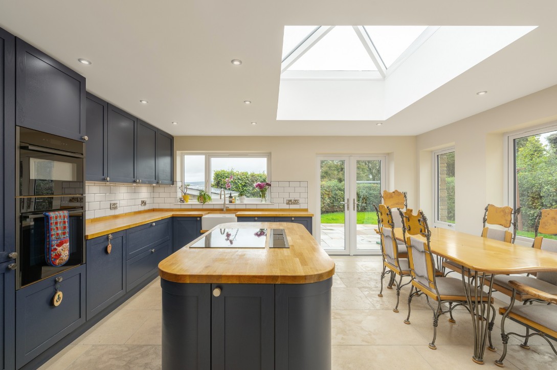 Dark blue shaker kitchen with oak worktops, central island, skylight and dining area by 21 Kitchens in Ayrshire.