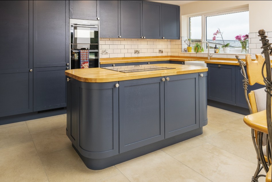Dark blue shaker kitchen with oak worktop island, integrated ovens and white metro tile splashback by 21 Kitchens in Ayrshire