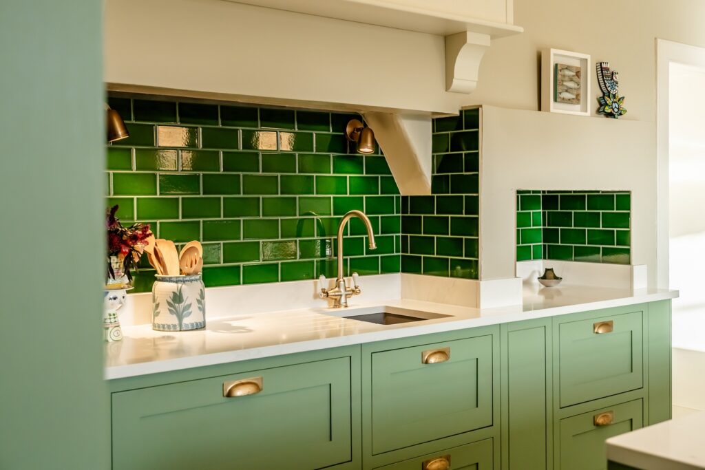 Green painted kitchen display with integrated ovens, white worktops and green metro tile splashback by 21 Kitchens.