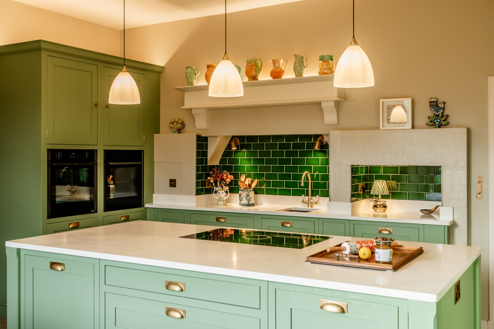 Green shaker kitchen showroom display with white worktops, brass handles and pendant lighting by 21 Kitchens in Ayrshire.