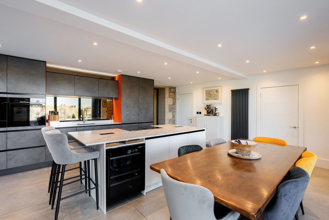 Grey bespoke kitchen with white island, breakfast seating and open-plan dining area by 21 Kitchens in Ayrshire.