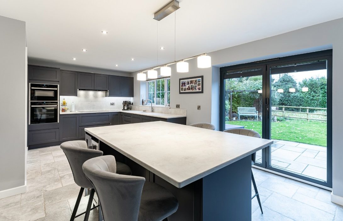 Grey German kitchen with large island, integrated ovens, pendant lighting and garden doors by 21 Kitchens in Ayrshire.