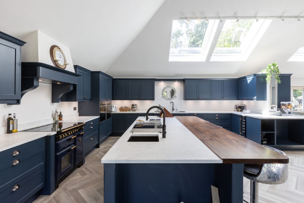 Luxury blue kitchen with skylight windows, large island, marble-effect worktop, wooden breakfast bar and herringbone flooring by 21 Kitchens in Ayrshire.