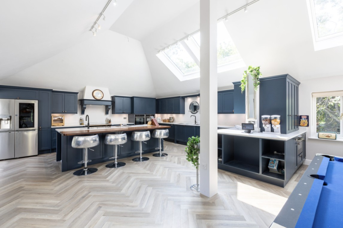 Luxury blue open-plan kitchen with large island, skylight windows, breakfast bar seating and herringbone flooring by 21 Kitchens in Ayrshire.