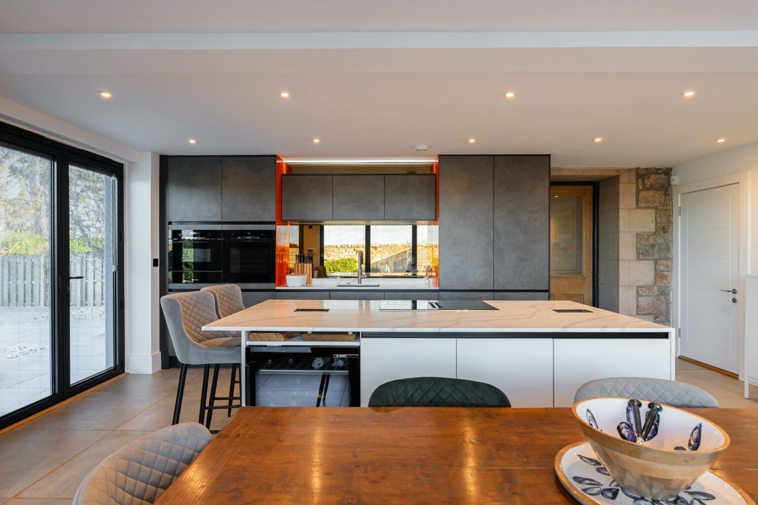 Modern bespoke kitchen with large island, grey cabinetry and open-plan dining area by 21 Kitchens in Ayrshire.