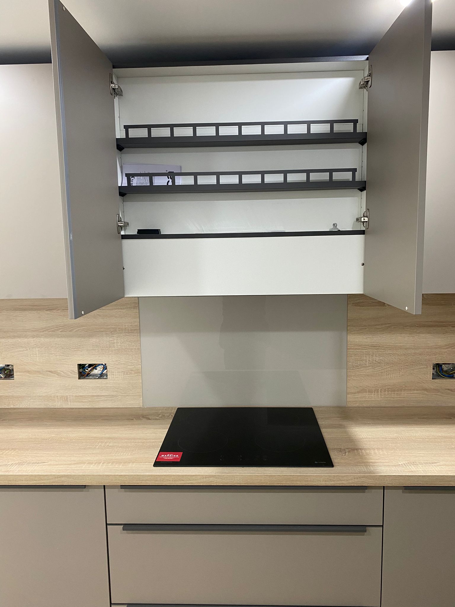 Contemporary taupe kitchen with induction hob, wood effect worktop and overhead storage by 21 Kitchens