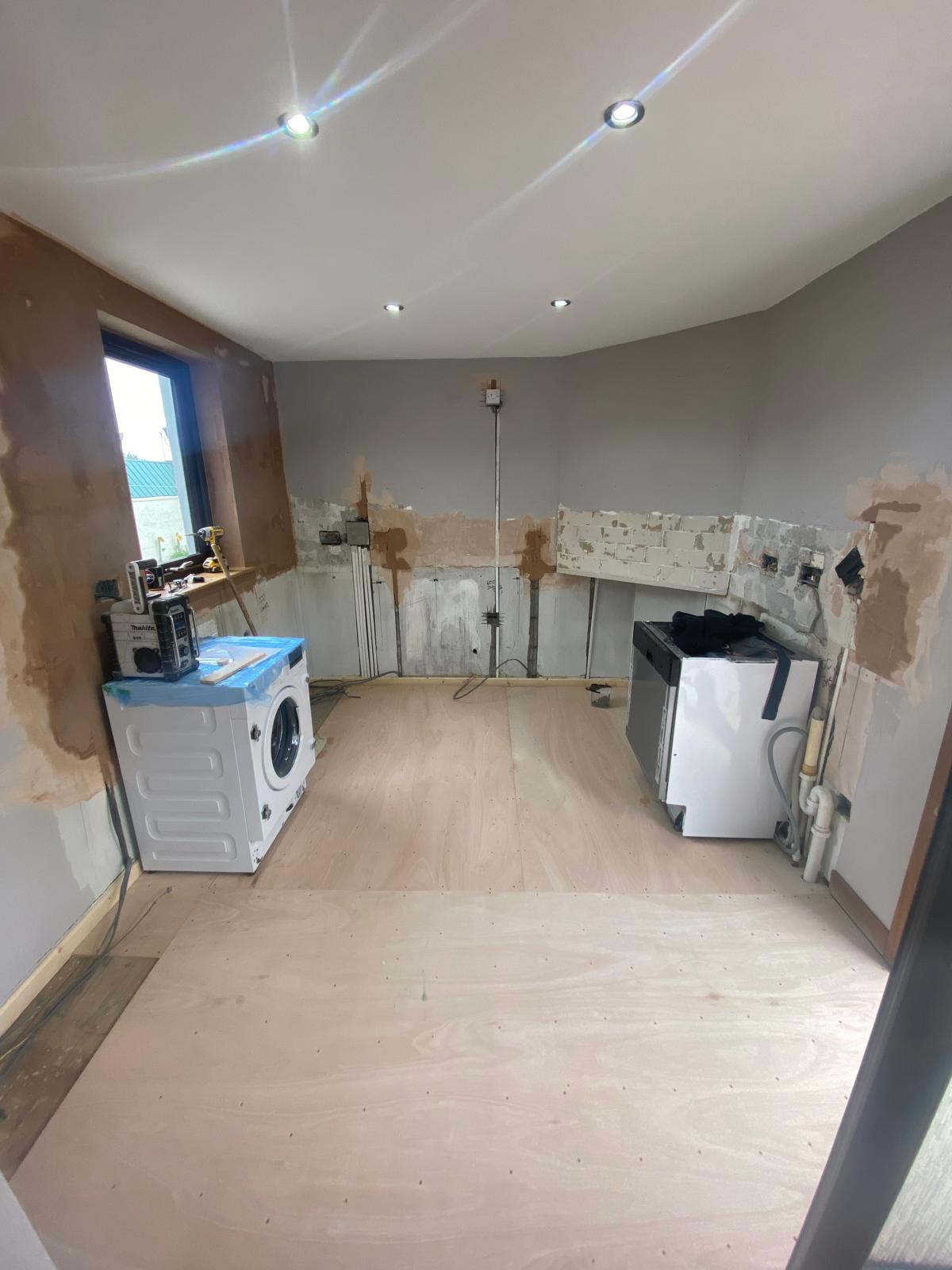 Kitchen before renovation with stripped walls, exposed services and flooring prepared for fitted kitchen installation.