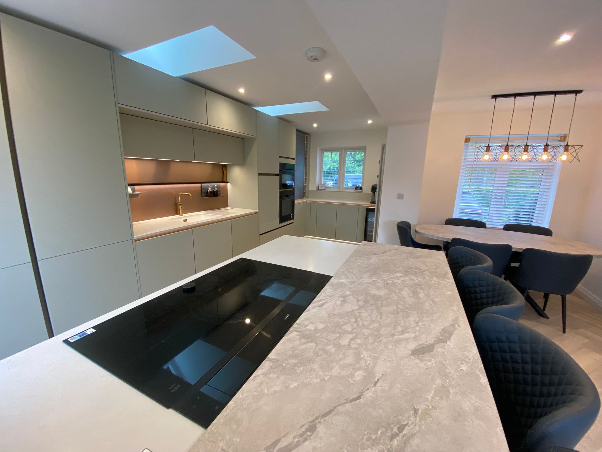 Modern sage green kitchen island with induction hob, stone-effect worktop and open-plan dining area in Ayrshire.