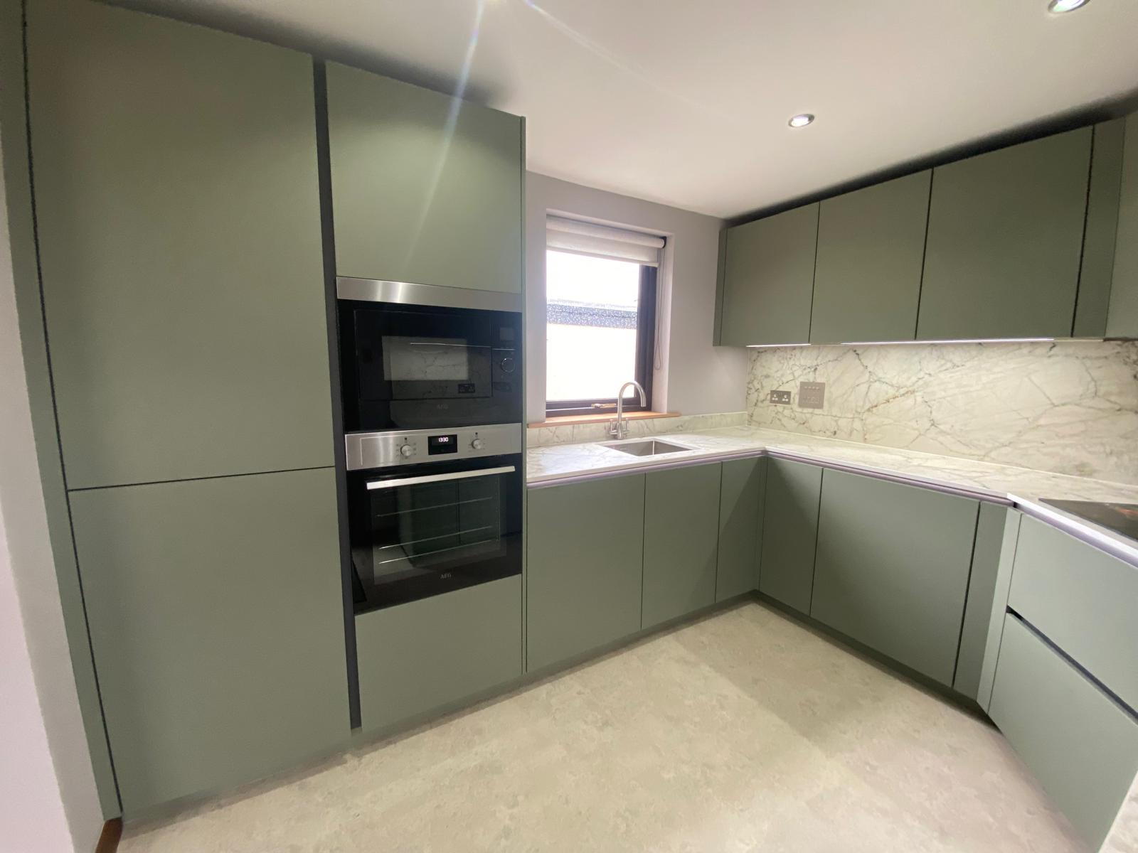 Modern sage green U-shaped kitchen with marble-effect splashback, integrated appliances and ceiling spotlights.