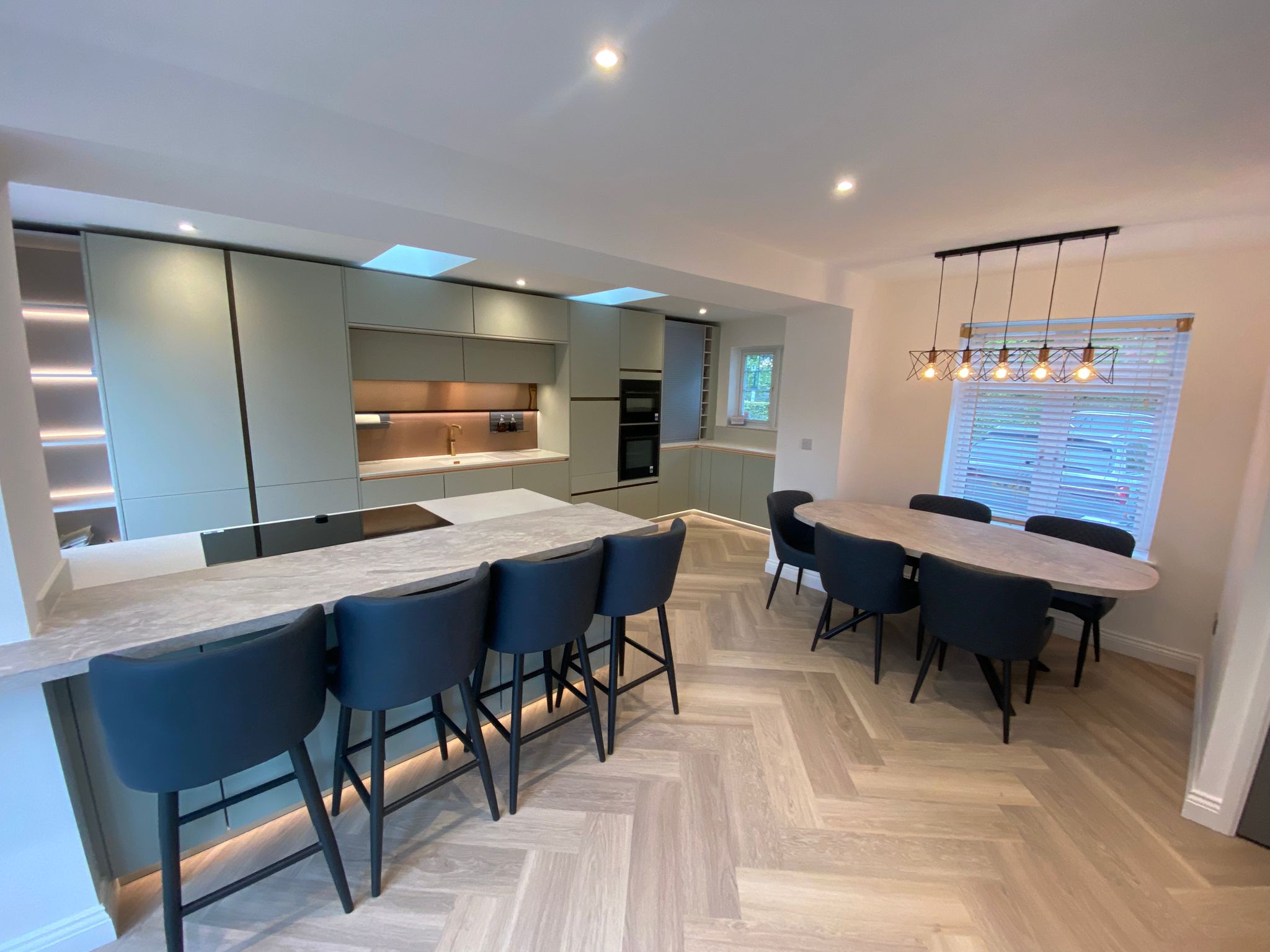 Open-plan sage green kitchen with island seating, dining area and modern lighting in Ayrshire.