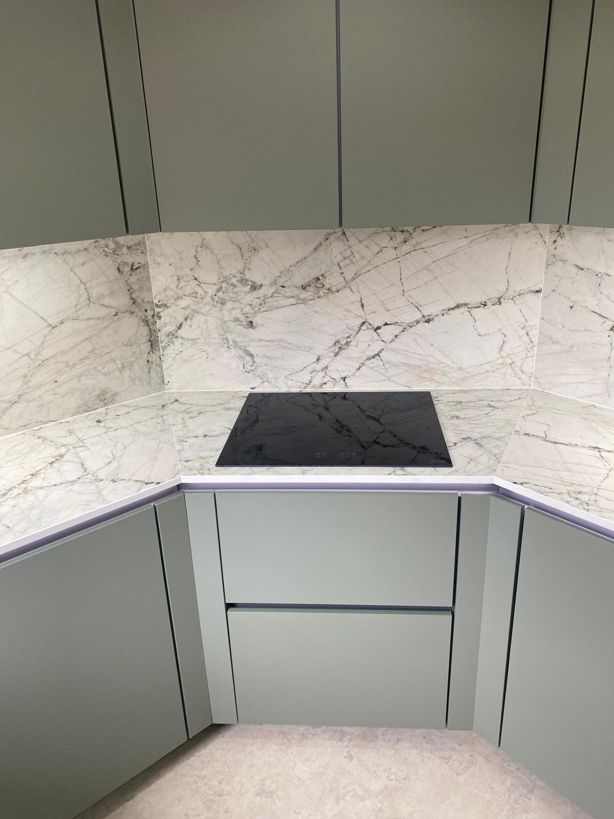 Sage green kitchen with induction hob, marble-effect worktop and matching marble splashback.