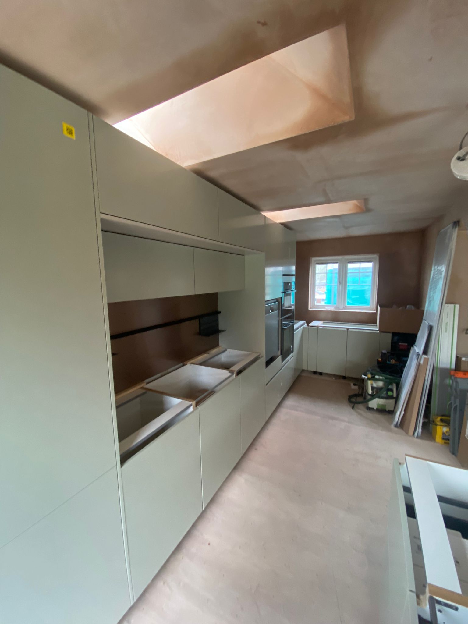 Sage green fitted kitchen installation in progress with tall units, rooflights and integrated appliances.