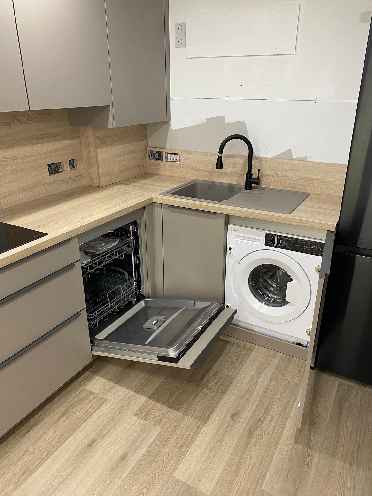 Taupe fitted kitchen sink area with integrated dishwasher, washing machine space and black tap